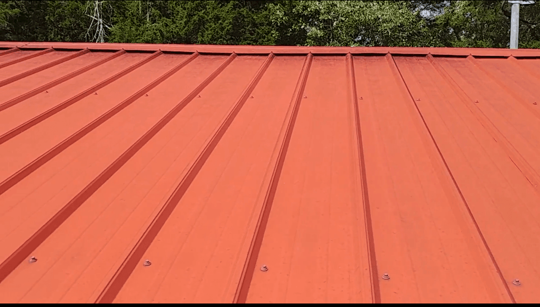 A professional tightening a screw on a metal roof panel.